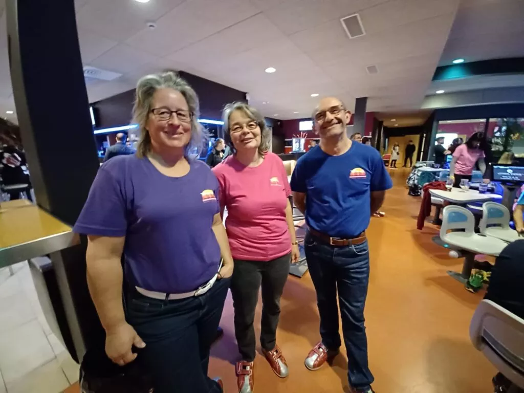 Trois personnes en chemises violettes debout dans une piste de bowling.