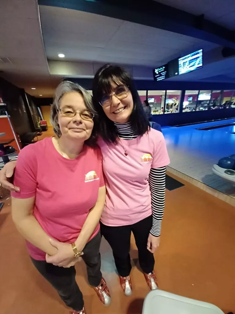 Deux femmes en chemises roses debout l'une à côté de l'autre dans une piste de bowling.