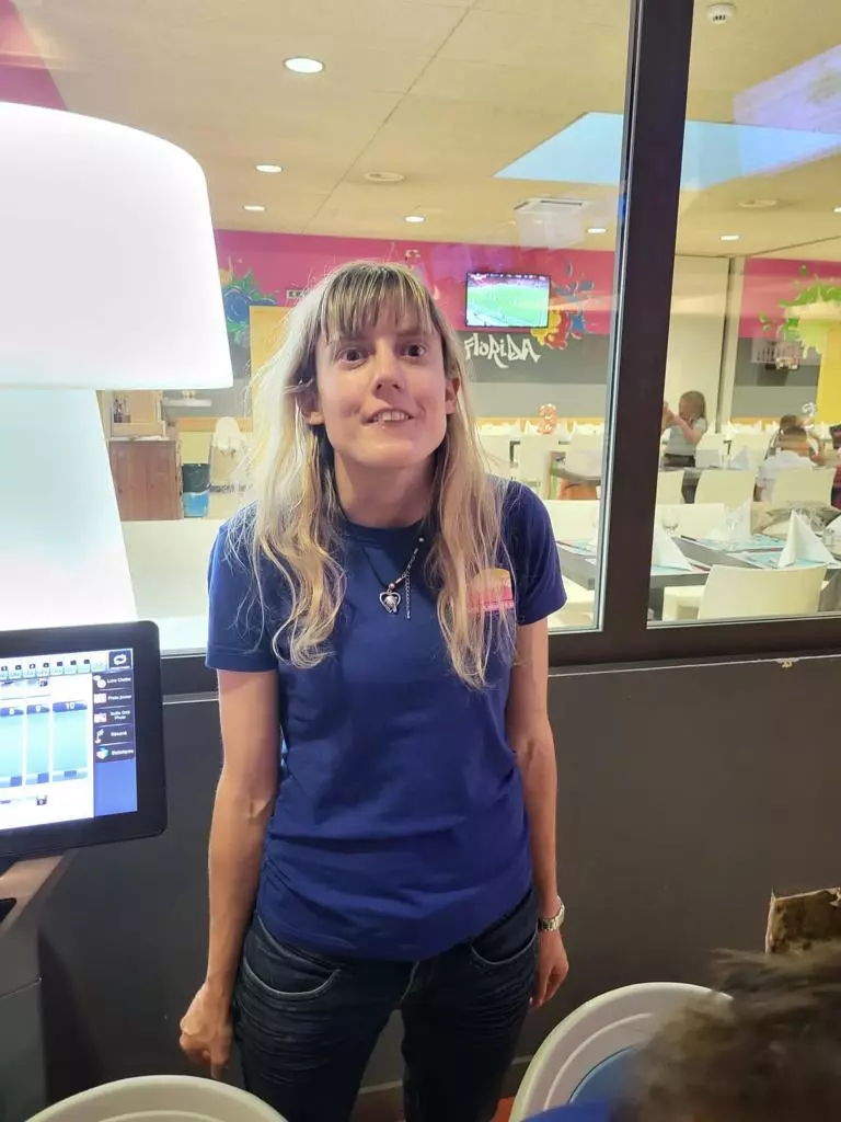 Une femme en chemise bleue debout devant une fenêtre.