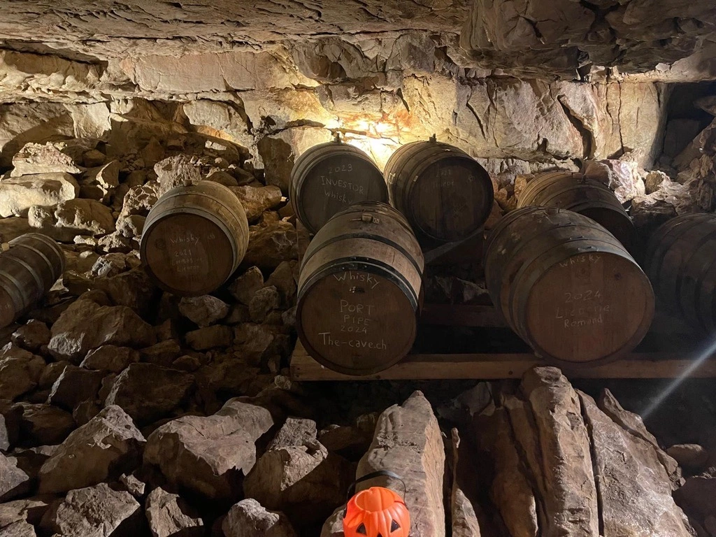 Fûts de whisky vieillissant dans une cave rocheuse et faiblement éclairée avec des façades étiquetées indiquant le contenu et les dates.