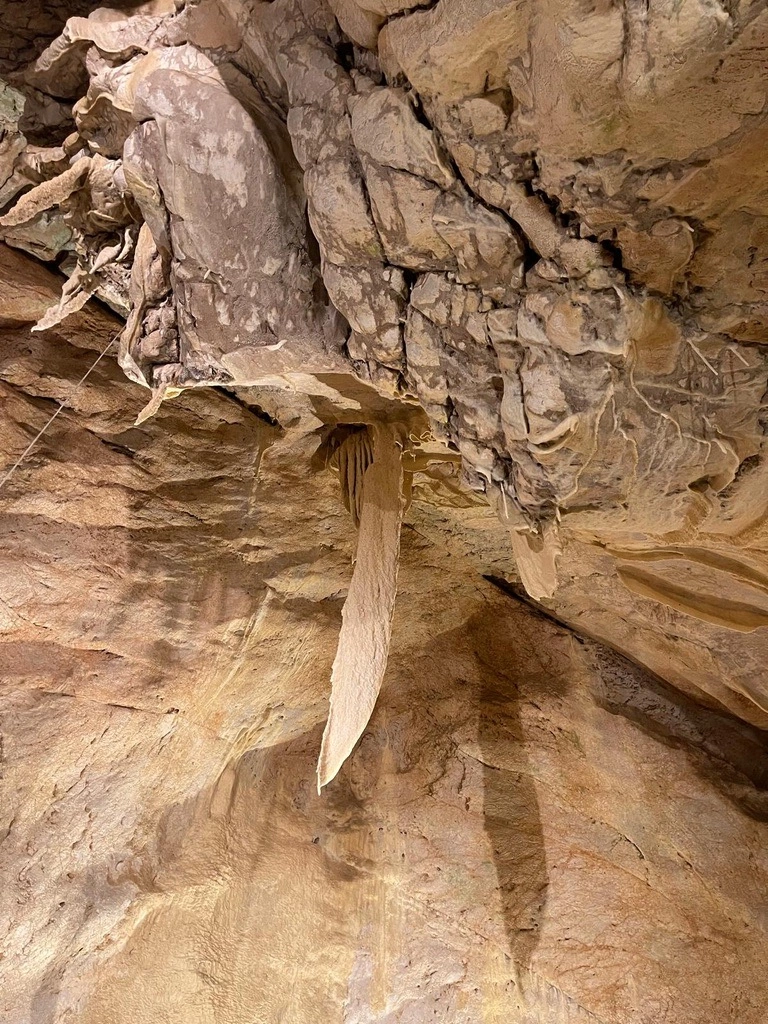 Une formation rocheuse naturelle avec une protubérance proéminente et déchiquetée vers le bas du plafond de la grotte, sur fond de mur texturé.
