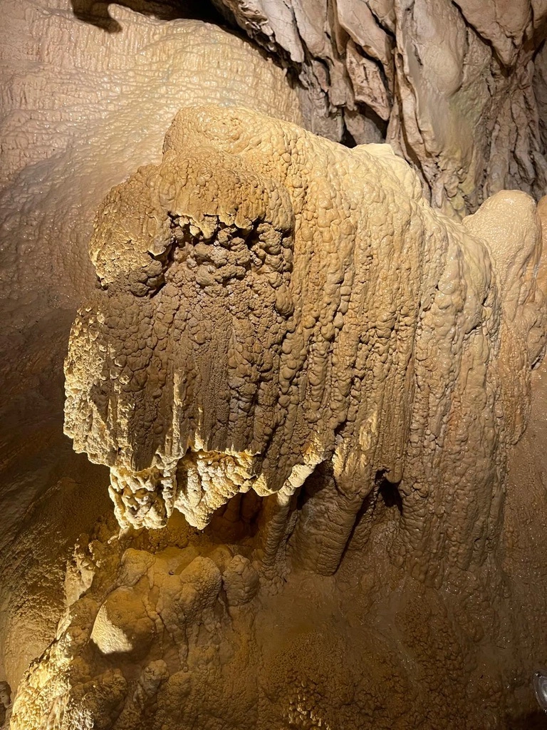 Gros plan d'une formation rocheuse à l'intérieur d'une grotte, présentant des motifs texturés et superposés dans une teinte brune, avec des surfaces rugueuses et déchiquetées éclairées par la lumière.