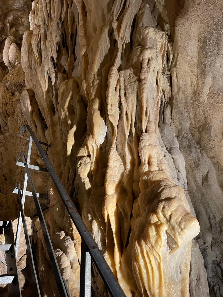 Une formation rocheuse dans une grotte avec des stalactites, à côté d'une balustrade métallique.