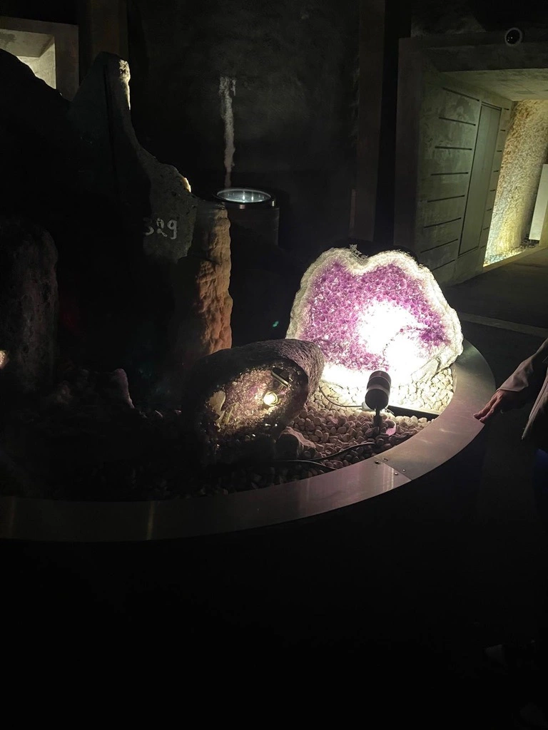 Une grande géode d'améthyste est exposée avec un projecteur dans une pièce faiblement éclairée.