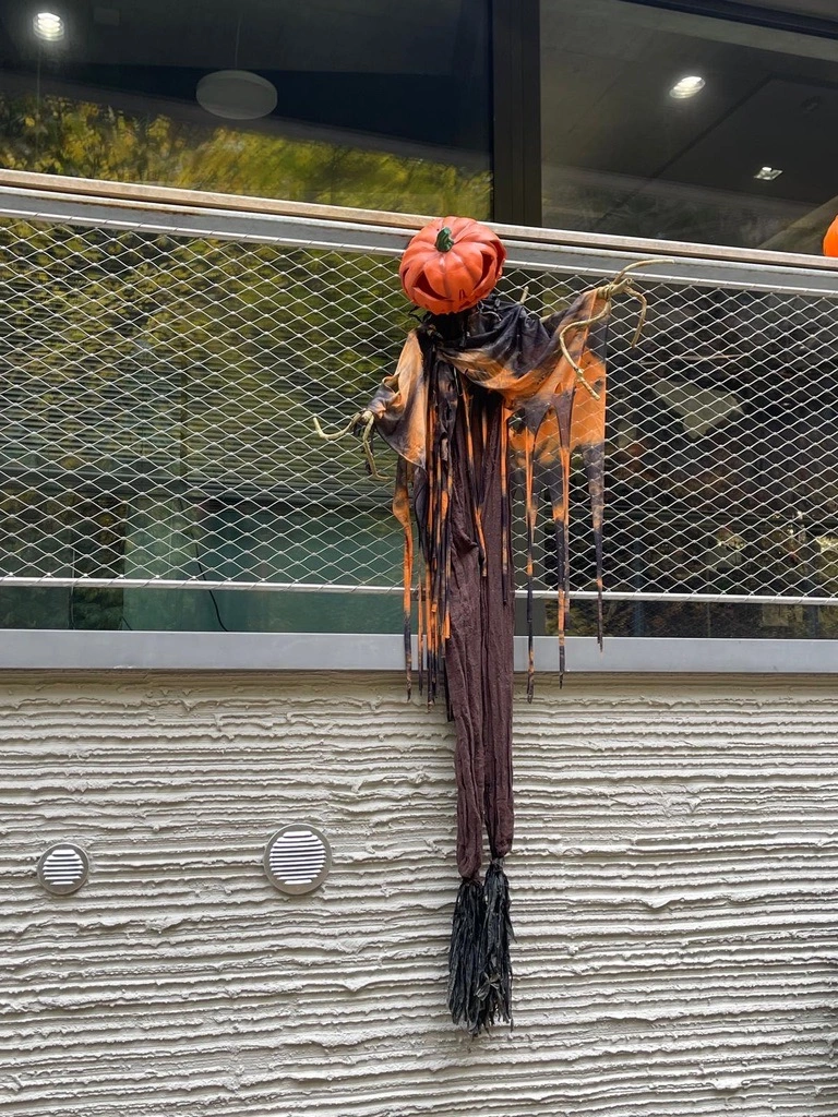 Une décoration en forme de tête de citrouille avec du tissu noir et orange en lambeaux est accrochée à une balustrade en métal à l'extérieur d'un bâtiment.