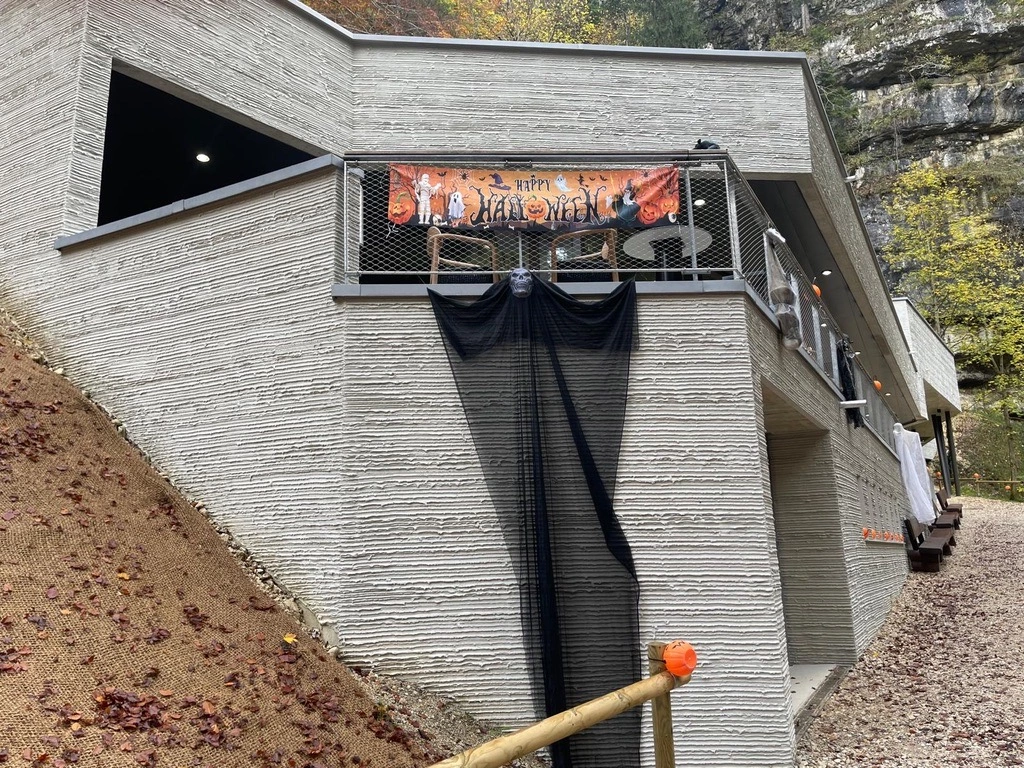 Bâtiment en béton avec une bannière d'Halloween et un tissu noir suspendu au balcon. Il y a une pente de terre à côté du bâtiment et une falaise rocheuse en arrière-plan.