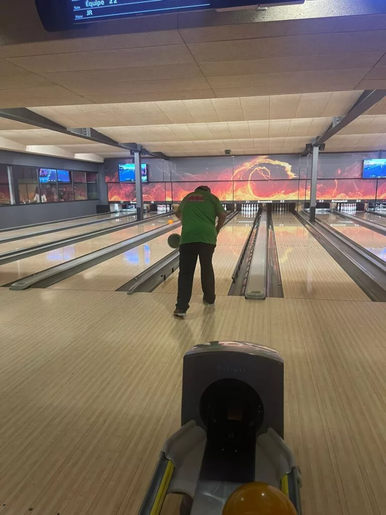 Une personne joue au bowling et se prépare à lancer la boule sur la piste dans une salle de bowling intérieure.