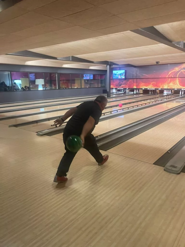 Une personne joue au bowling sur une piste avec une boule de bowling verte dans un bowling intérieur. La boule est sur le point de toucher les quilles.