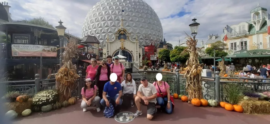 Un groupe de personnes pose devant un dôme géodésique dans un parc d'attractions, entouré de citrouilles et de décorations d'automne.
