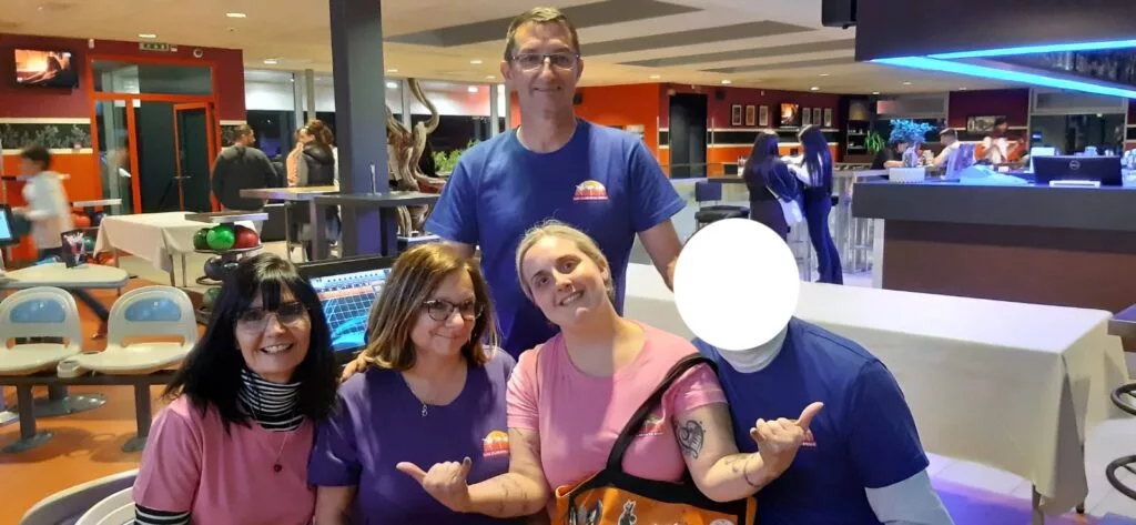 Cinq personnes posant dans un bowling, portant des chemises colorées. Le visage d'une personne est caché.