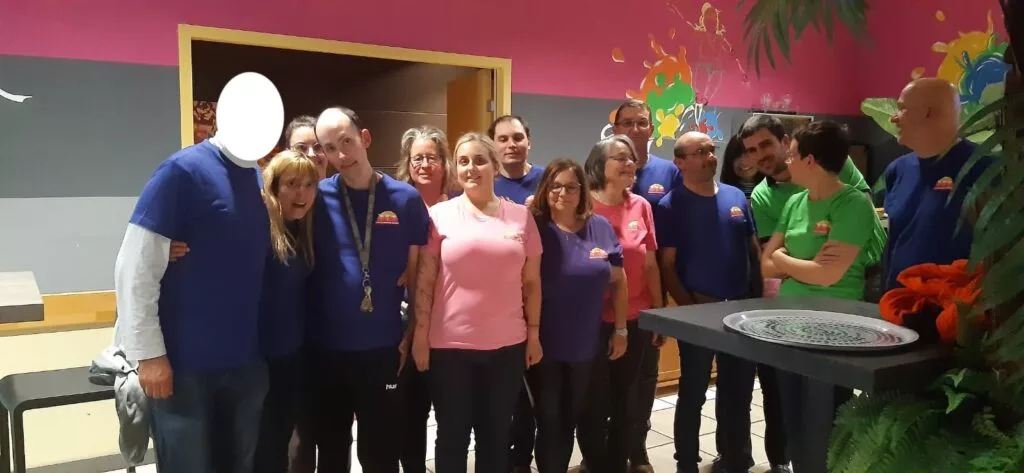Un groupe de personnes portant des chemises colorées se tiennent ensemble dans une pièce aux murs vibrants, certaines souriant à la caméra.