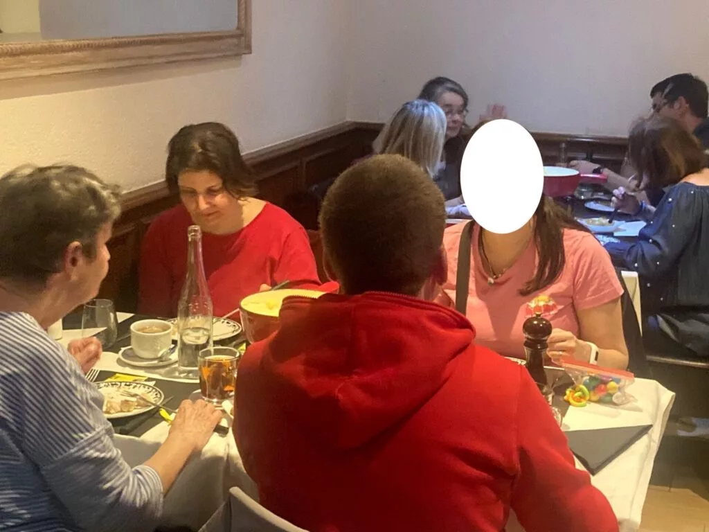 Des gens assis à une table de restaurant mangent et discutent, avec divers plats et boissons sur la table.