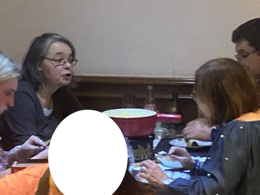 Groupe de personnes assises à une table, partageant un repas avec un caquelon à fondue au centre.
