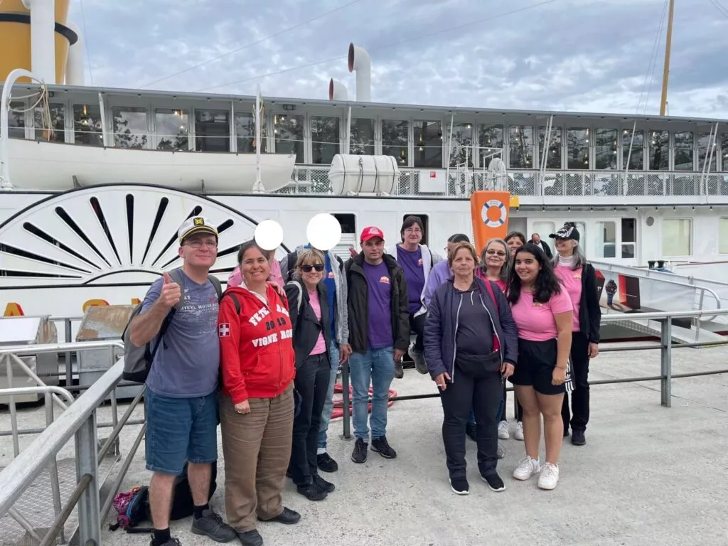 Un groupe de personnes debout sur un quai devant un grand bateau blanc, avec un ciel nuageux au-dessus.