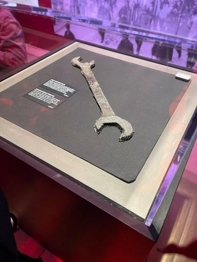 Une vieille clé rouillée exposée dans une vitrine en verre dans un musée avec une plaque d'information à côté.