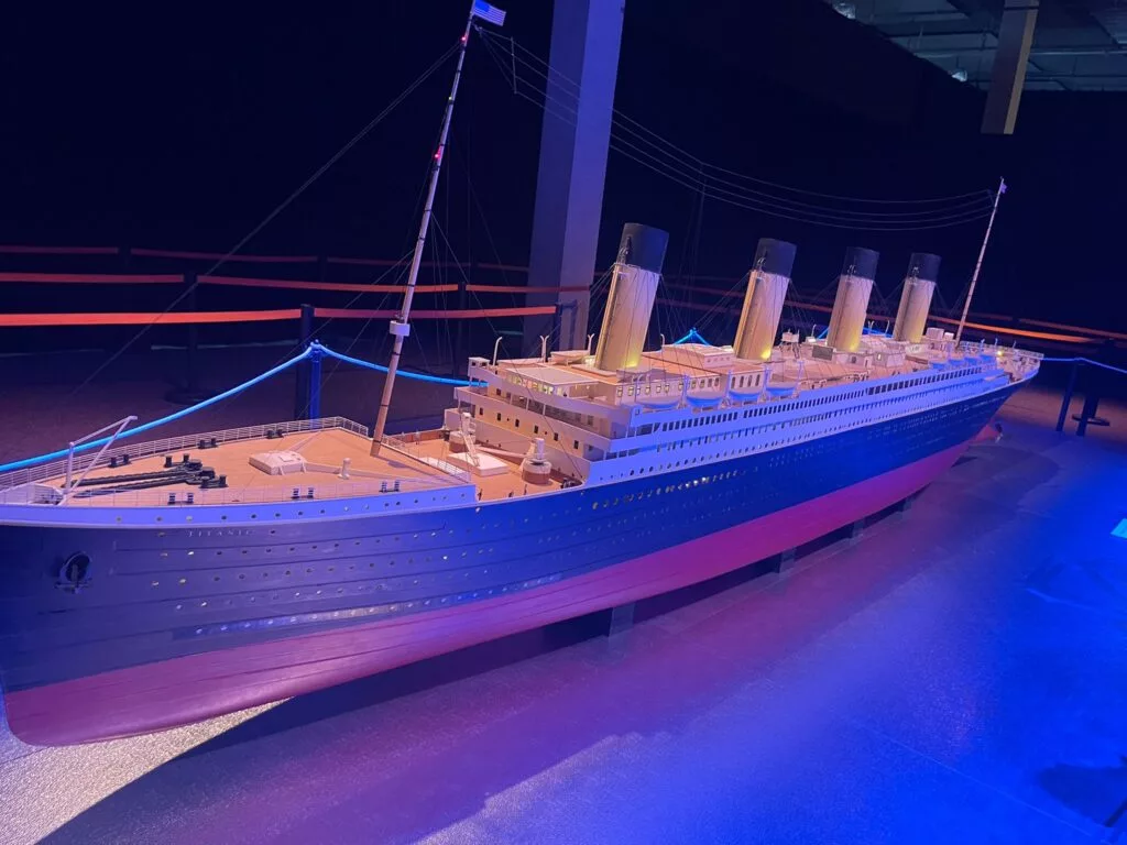 Maquette du navire Titanic exposée à l'intérieur, éclairée sous un éclairage bleu, avec des éléments détaillés comme des cheminées et des canots de sauvetage visibles.