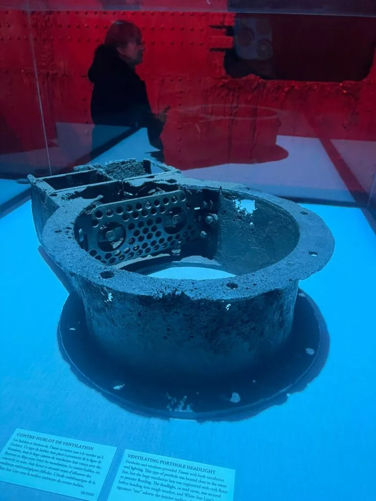 Objet métallique circulaire rouillé exposé dans une vitrine en verre, accompagné de plaques d'information.