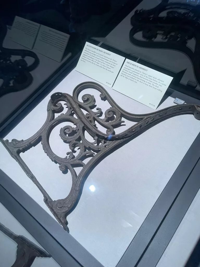 Un support métallique décoratif et orné présenté dans une vitrine en verre, avec des plaques descriptives en arrière-plan.