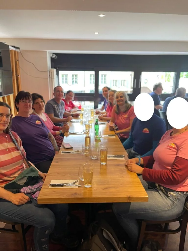 Un groupe de personnes assises autour d'une longue table en bois avec des boissons dans un restaurant. Les visages de deux personnes sont flous.