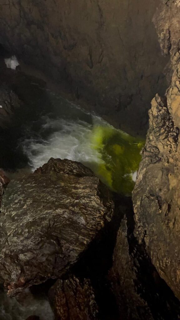 L'intérieur d'une grotte rocheuse avec de l'eau qui coule à travers, éclairé par un reflet de lumière verte sur la surface.
