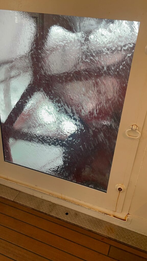 Fenêtre en verre dépoli aux motifs géométriques et cadre en métal, encastrée dans un plancher en bois.