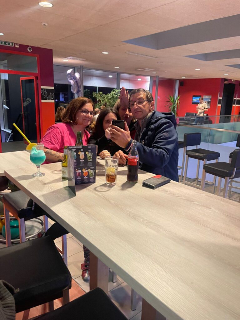 Un groupe de quatre personnes prenant un selfie à une table dans un café, avec des boissons sur la table et une décoration murale colorée en arrière-plan.