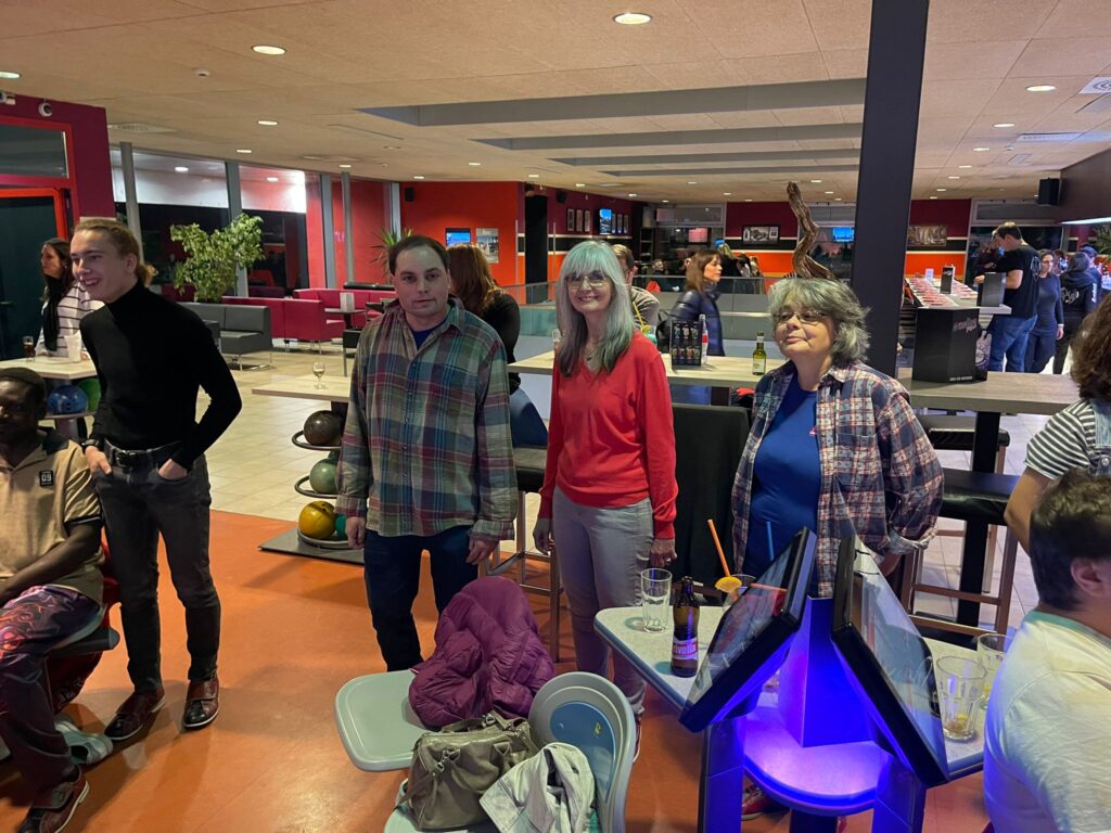 Un groupe de personnes debout ensemble dans une piste de bowling, avec des pistes et du matériel de bowling visibles en arrière-plan.