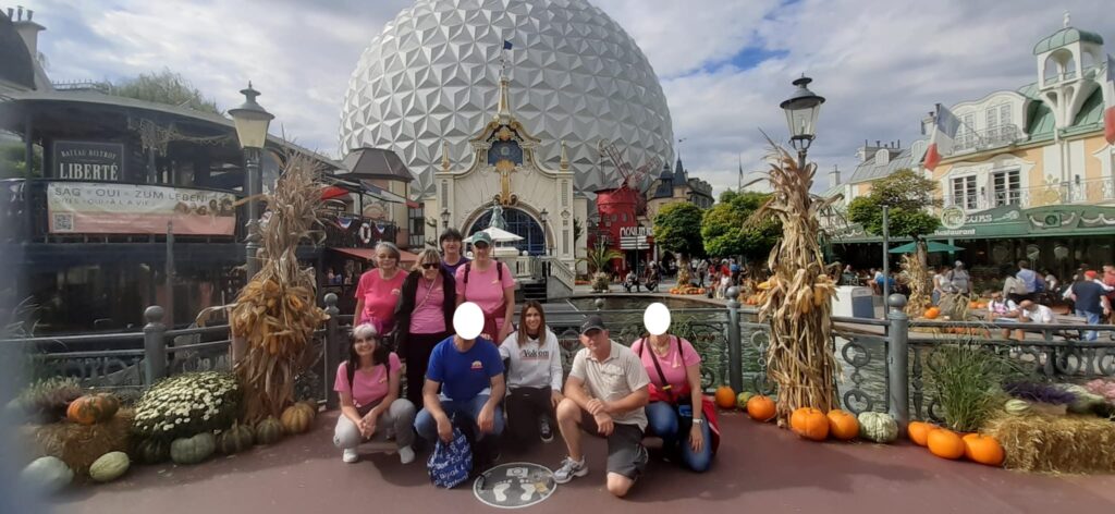 Un groupe de personnes pose devant un dôme géodésique dans un parc d'attractions, entouré de citrouilles et de décorations d'automne.
