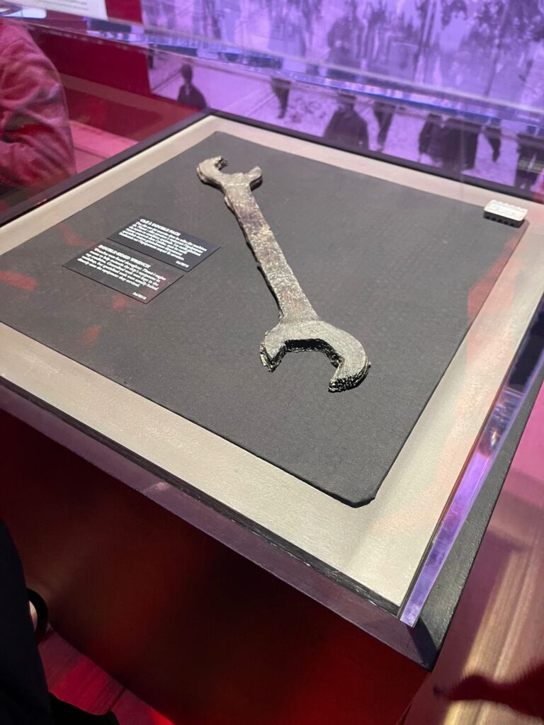 Une vieille clé rouillée exposée dans une vitrine en verre dans un musée avec une plaque d'information à côté.