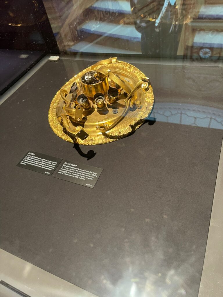Un artefact mécanique doré aux détails complexes affichés sur une surface noire, accompagné de panneaux d'information.