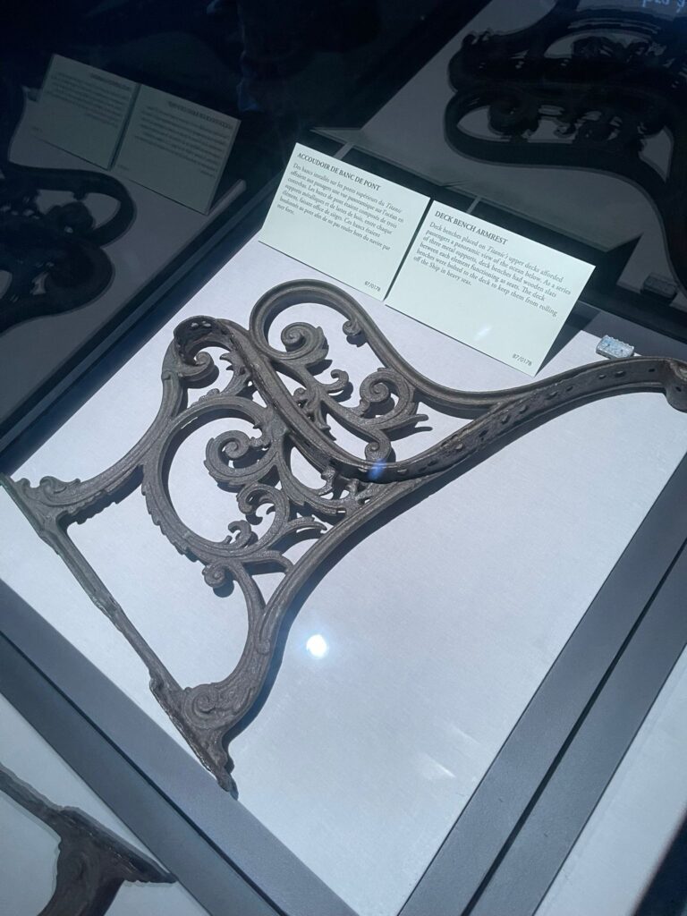 Un support métallique décoratif et orné présenté dans une vitrine en verre, avec des plaques descriptives en arrière-plan.